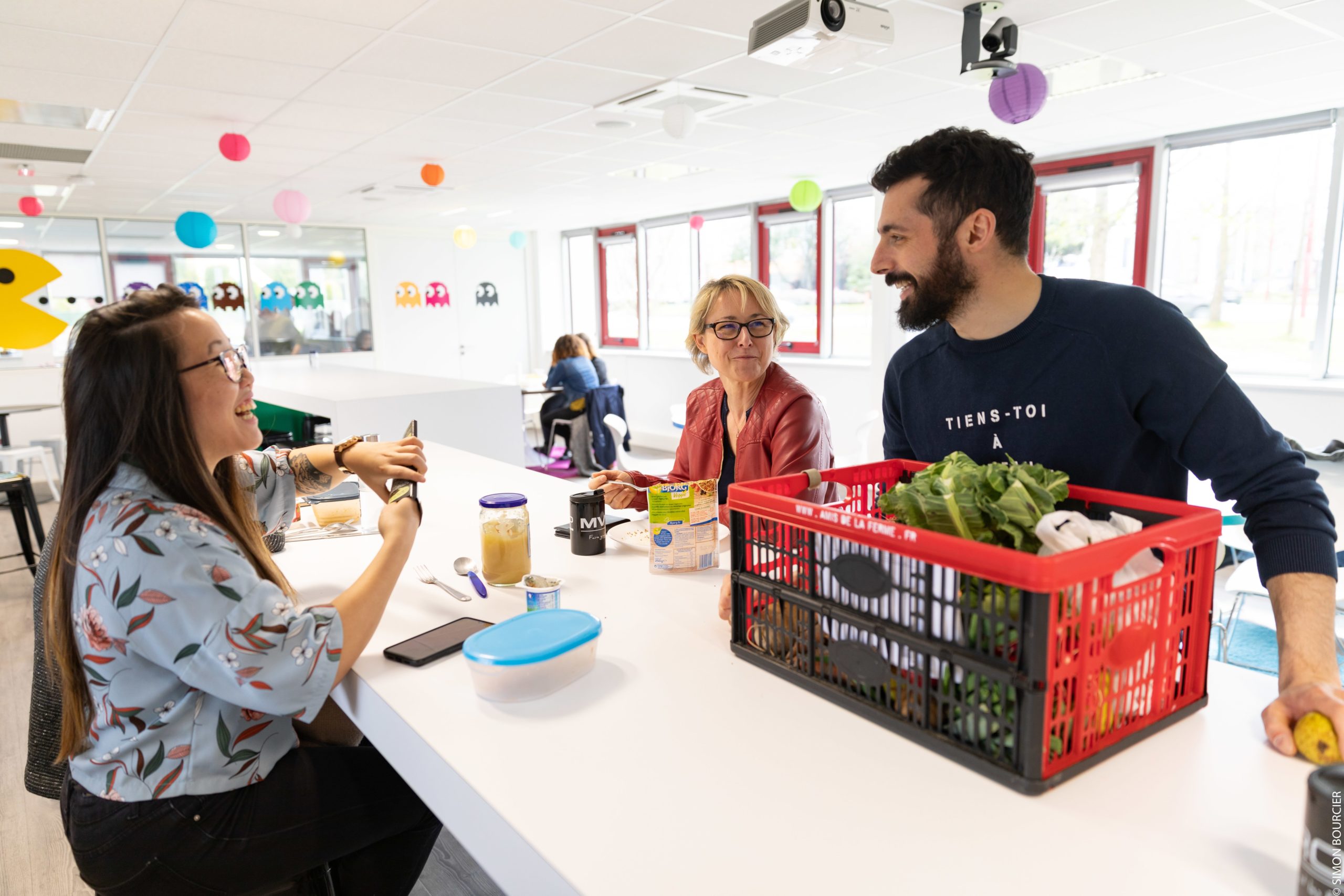Alexis, Happiness Manager, avec deux collaboratrices devant un panier de légumes dans la cafétéria de MV Group