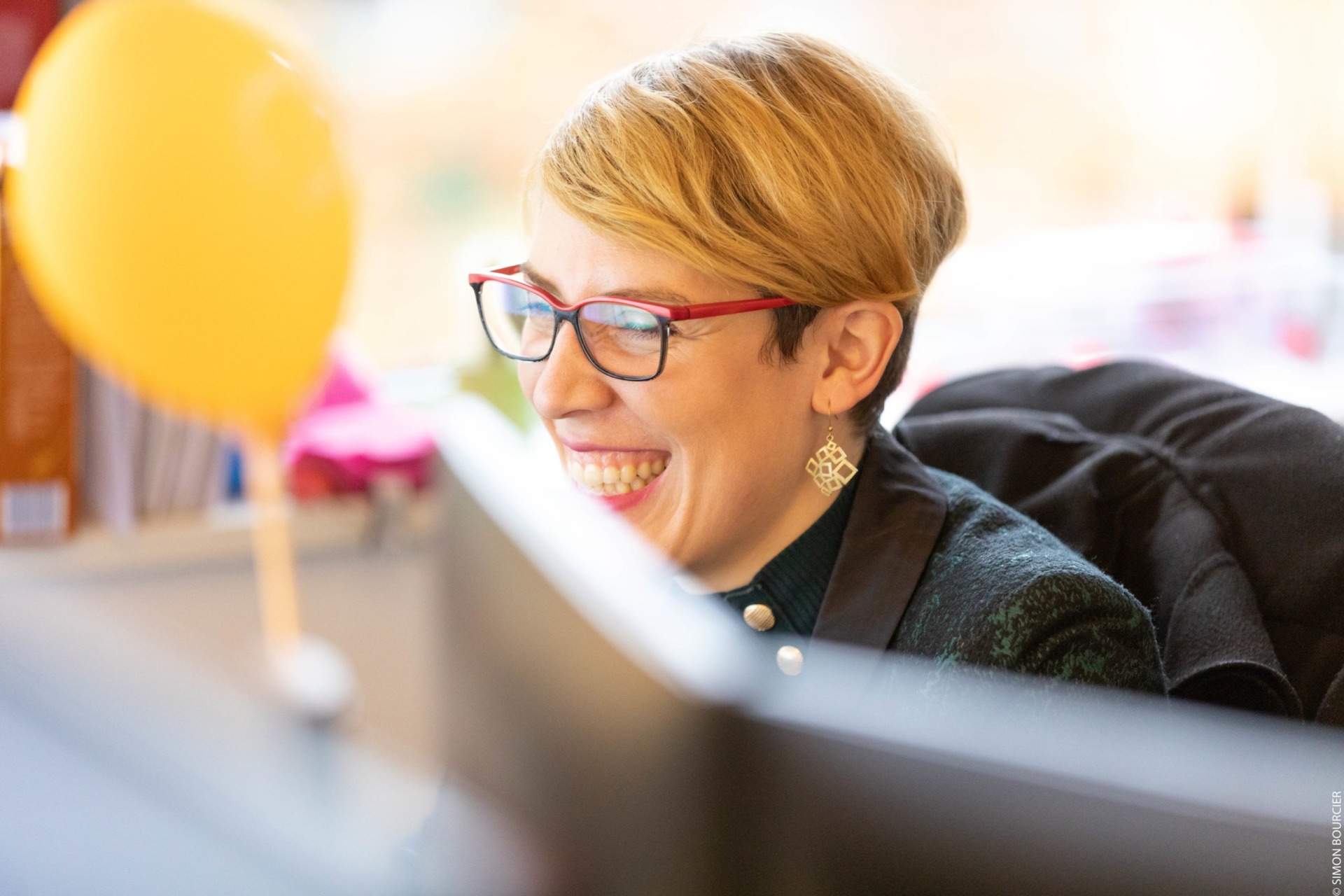 Collaboratrice souriant devant son écran, ballon jaune en arrière-plan